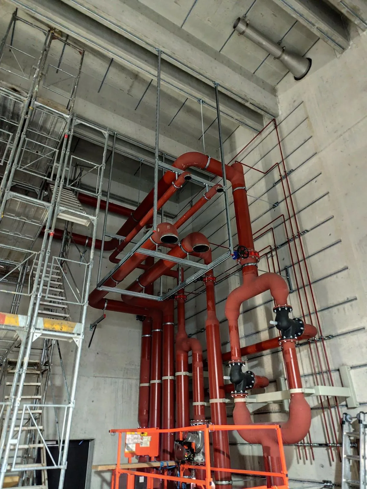 Installation of red industrial pipework beside scaffolding