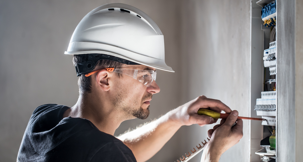 Man, an electrical technician working in a switchboard with fuses. Installation and connection of electrical equipment. Professional with tools in hand. concept of complex work, space for text.